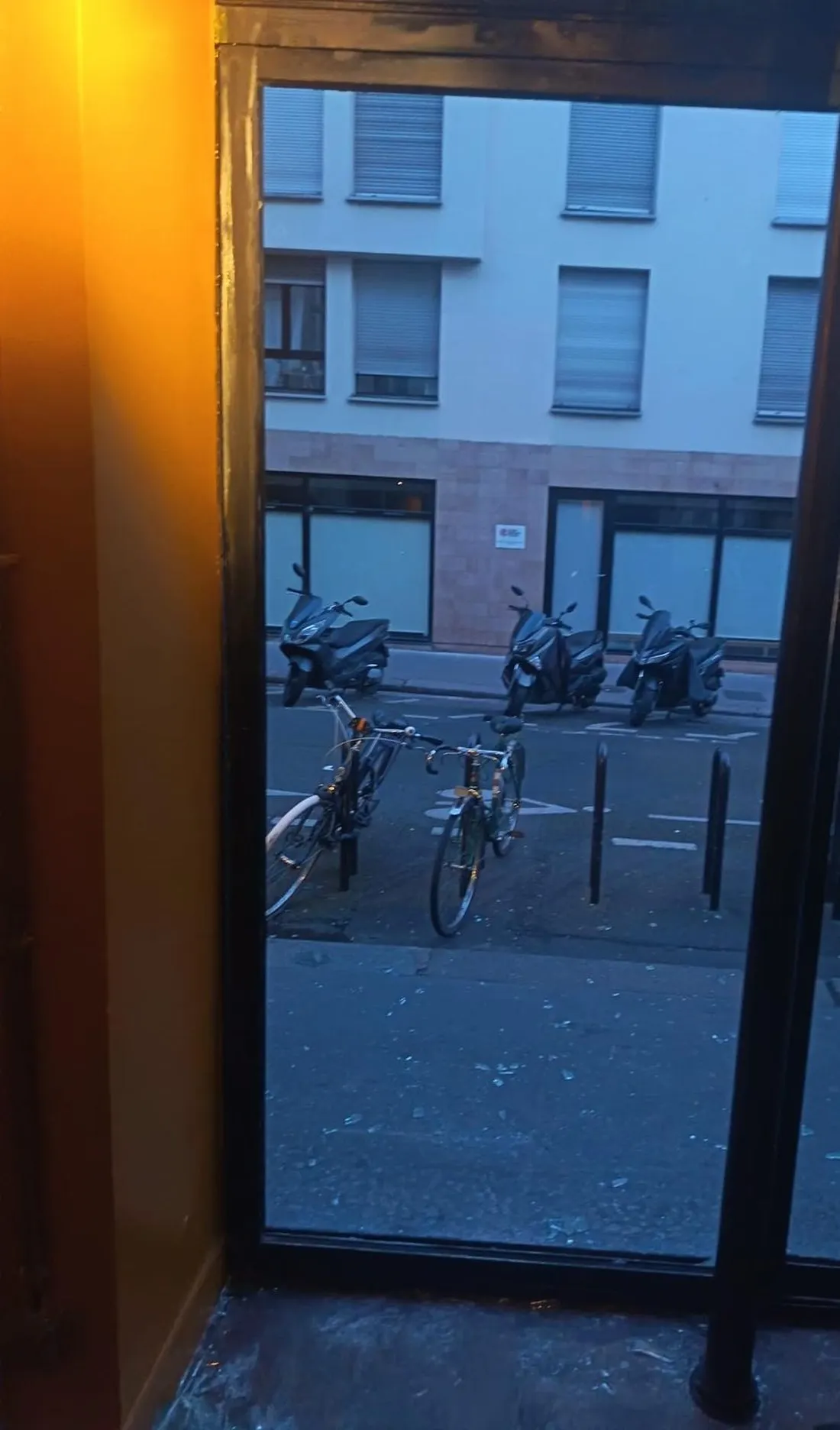 Baie de vitrine vide après dépose du vitrage brisé, éclats restant à déblayer sur le trottoir