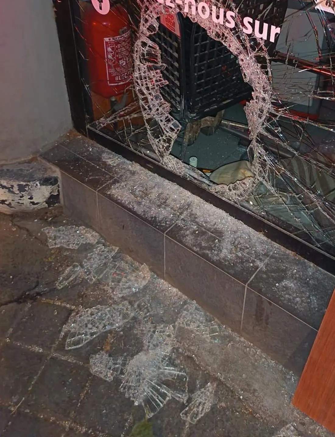 Glace feuilletée de devanture de commerce fracassée, impact traversant et éclats sur le trottoir